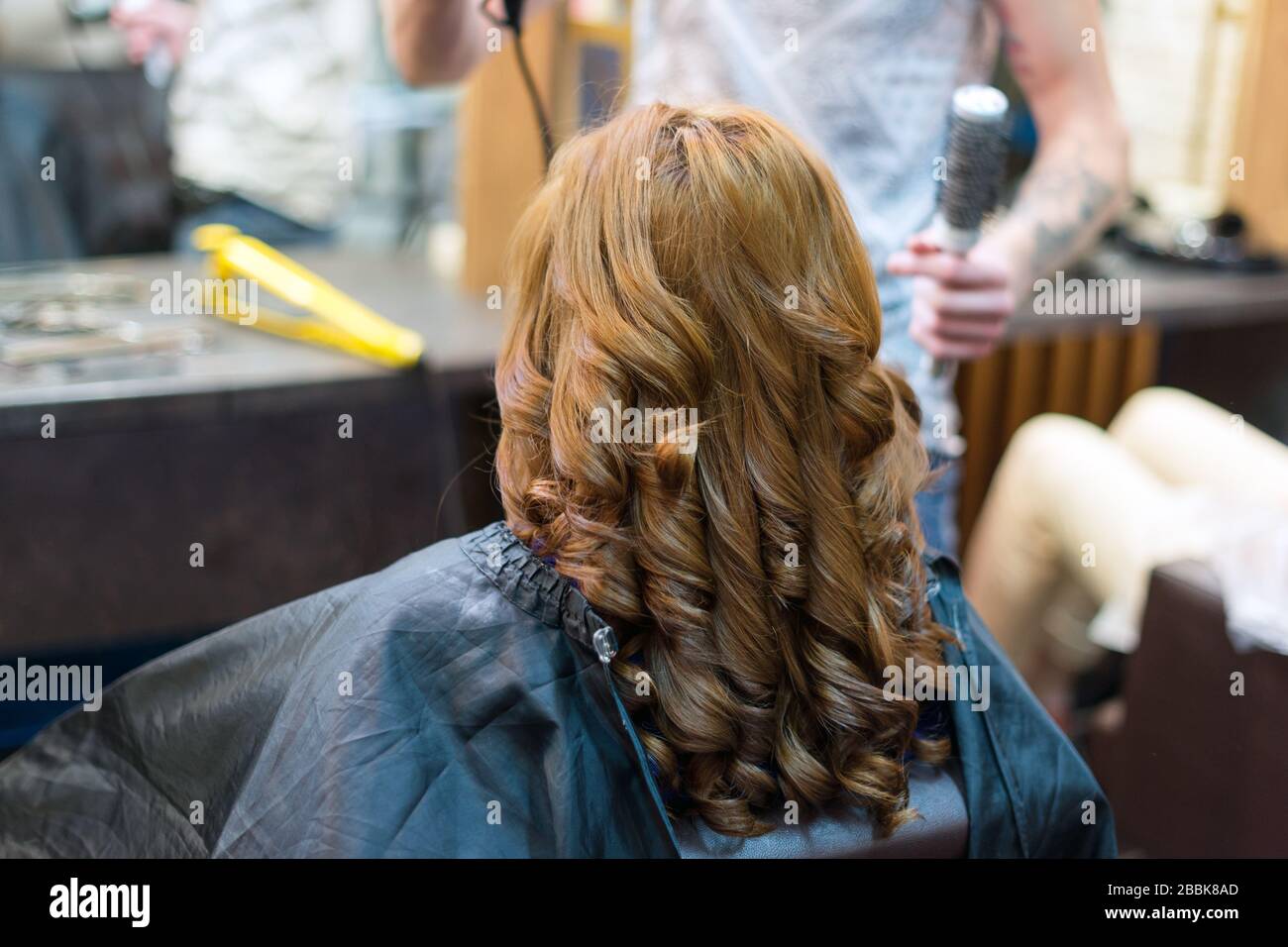 Parrucchiere usando un ferro arricciacapelli per impresa boccoli di capelli  lunghi marrone di un client femmina Foto stock - Alamy