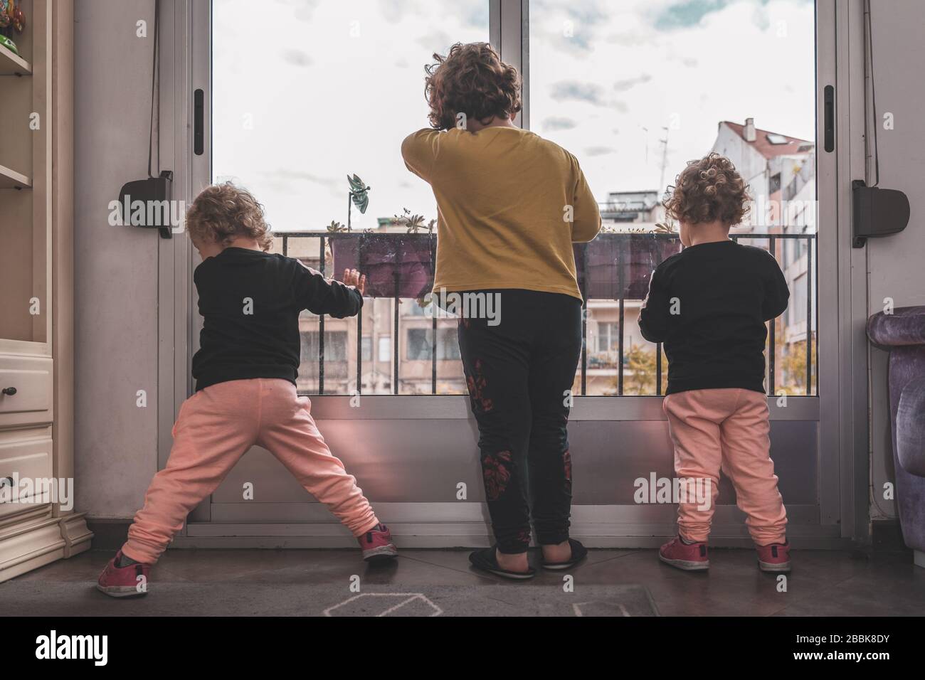 Un ragazzo e le sue due sorelle gemelle appoggiate contro la finestra rattristarono che non possono uscire al parco a causa del confinamento. Foto Stock