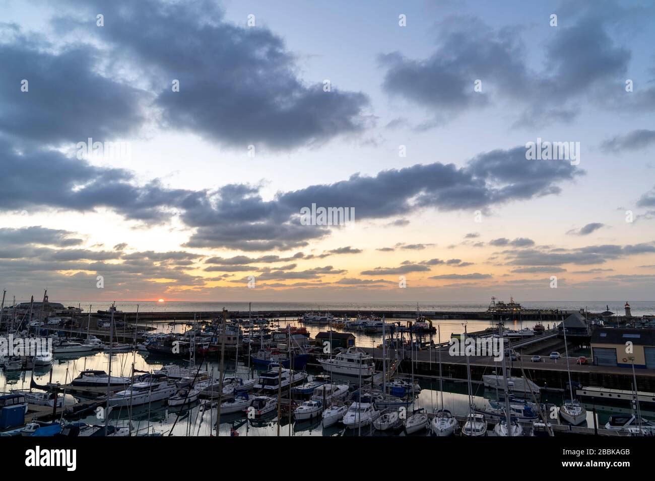 Alba sul porto di Ramsgate e il canale della Manica. Porto in primo piano con marina da diporto, sullo sfondo il sole che sorge sopra il mare in un cielo sparso di nuvole scure. Foto Stock