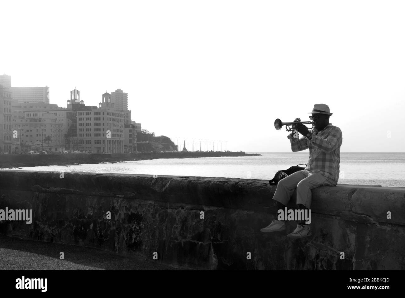 HAVANA, CUBA - 1 APRILE 2017: Musicista di strada cubana maschio nero con cappello e occhiali da sole che suonano la tromba seduto sul Malecon a l'Avana Foto Stock
