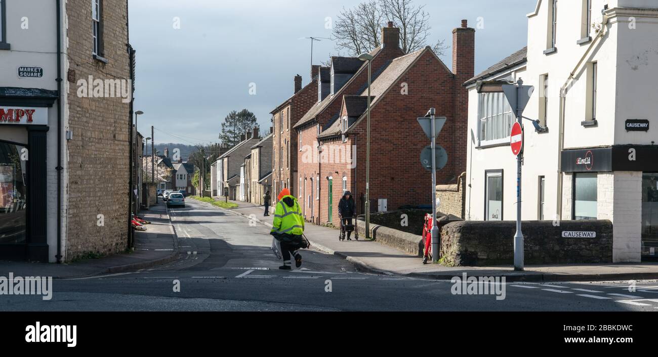 Un addetto alla pulizia delle strade che fornisce servizi essenziali attraversa un incrocio deserto. COVID Times. Bicester Town Centre, Oxfordshire, Regno Unito Foto Stock