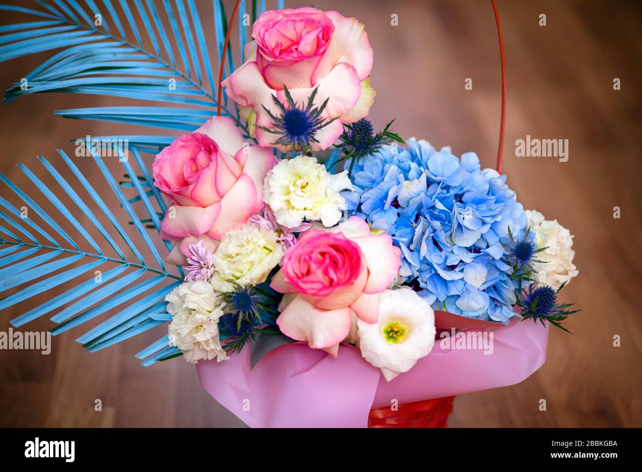 Bella composizione floreale con rose, eustoma e hydrangea nel cesto. Sfondo in legno. Foto Stock