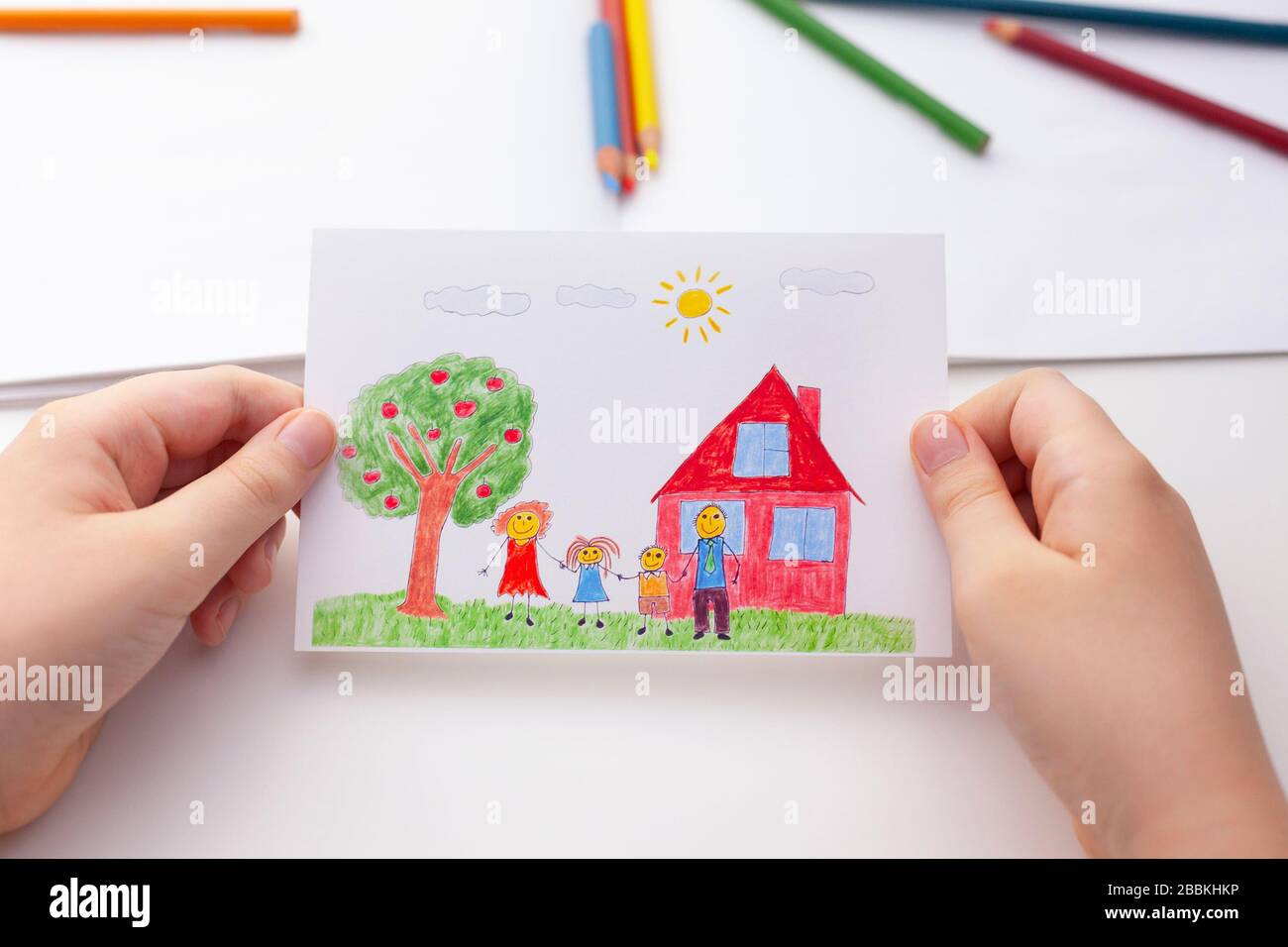 Bambino che tiene un disegno con una famiglia felice e un albero della mela e una casa. Primo piano. Foto Stock