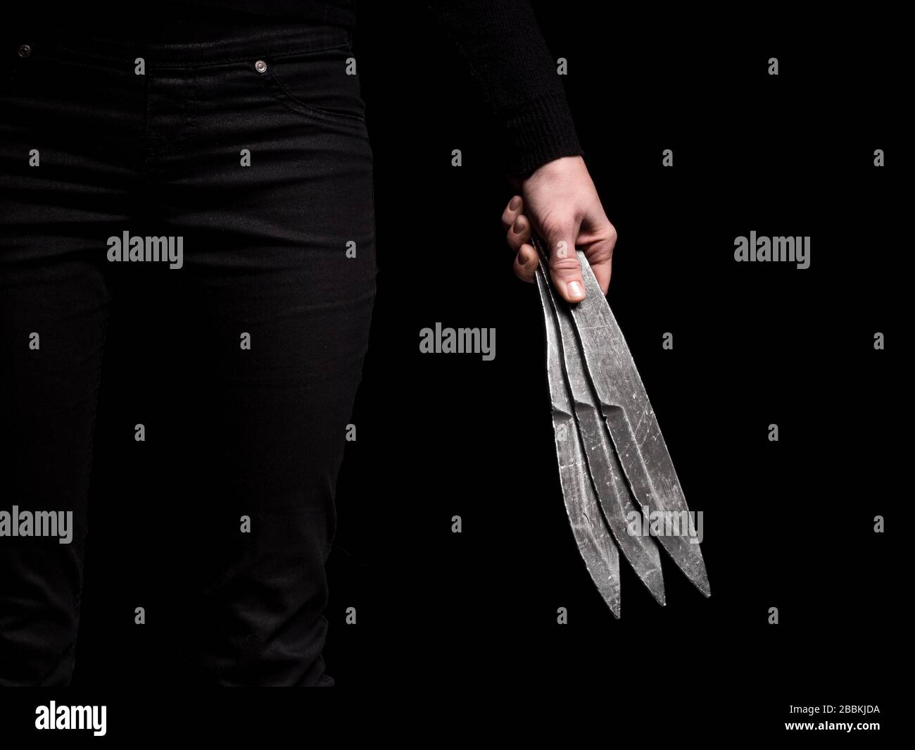 Ragazza che tiene in mano acciaio lancio coltelli su sfondo nero Foto Stock