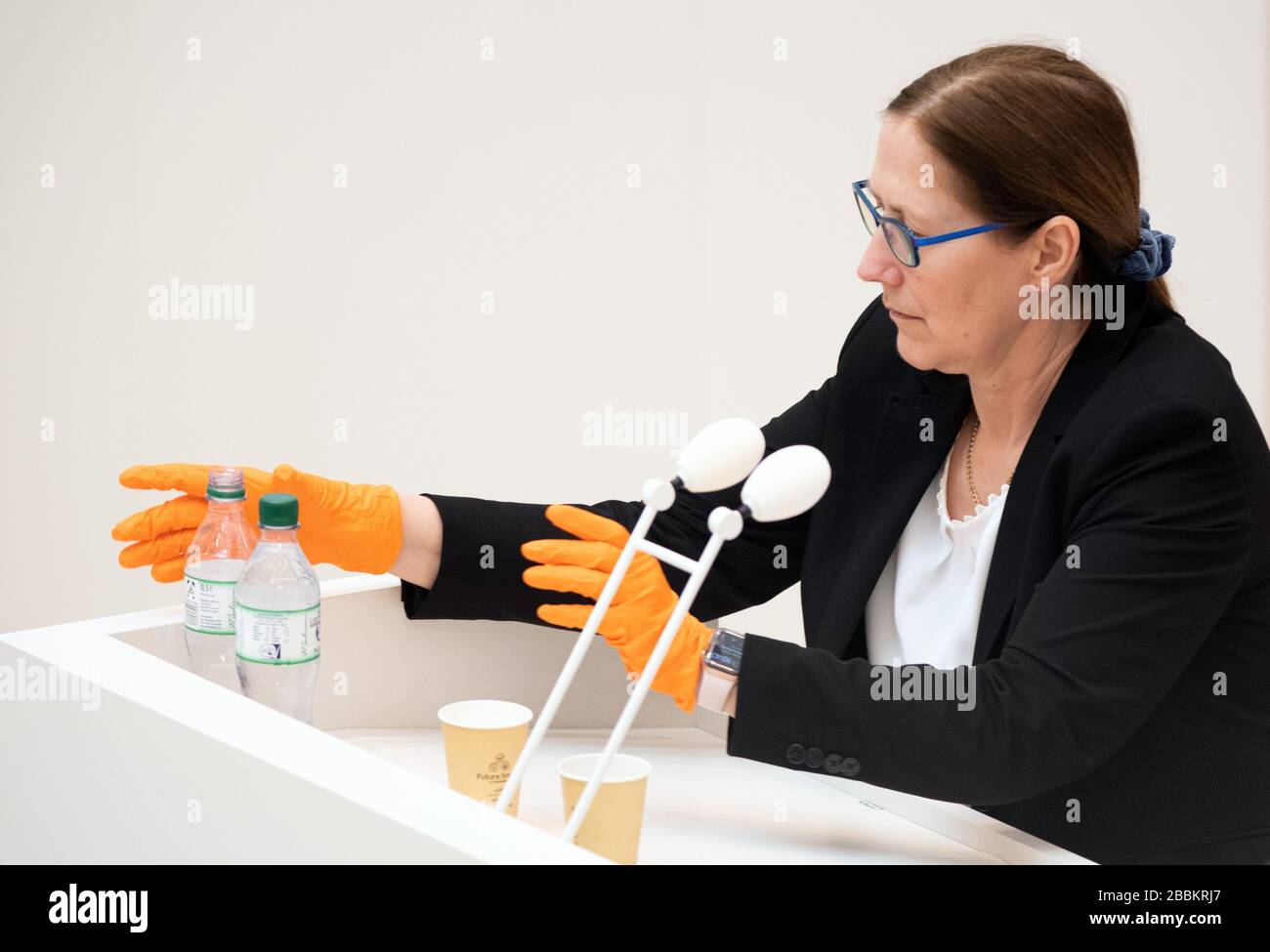 Potsdam, Germania. 01st Apr, 2020. Un membro del personale Landtag indossa guanti di protezione arancioni durante la sessione Landtag durante lo scambio di bottiglie di bevande sulla scrivania dell'altoparlante. Ulteriori sedie sono state aggiunte al Landtag nella sessione di Landtag dietro le file reali dei partiti parlamentari per mantenere la distanza minima tra le persone richieste a causa della crisi corona. Credito: Soeren Stache/dpa-Zentralbild/ZB/dpa/Alamy Live News Foto Stock