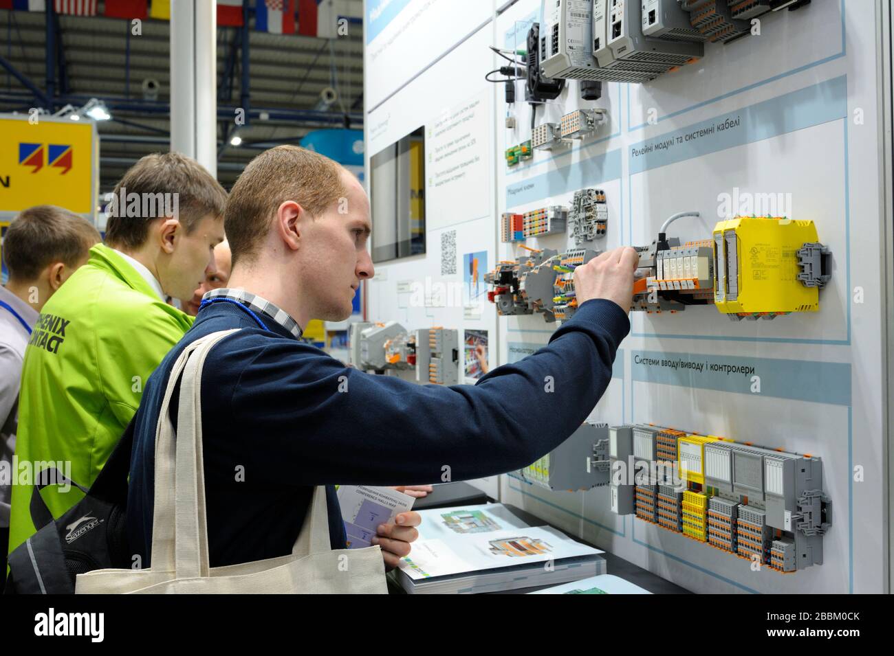 Il responsabile tocca il blocco del sistema di controllo automatico dell'alimentatore presentato sul supporto, spiegando al visitatore. Mostra industria Foto Stock