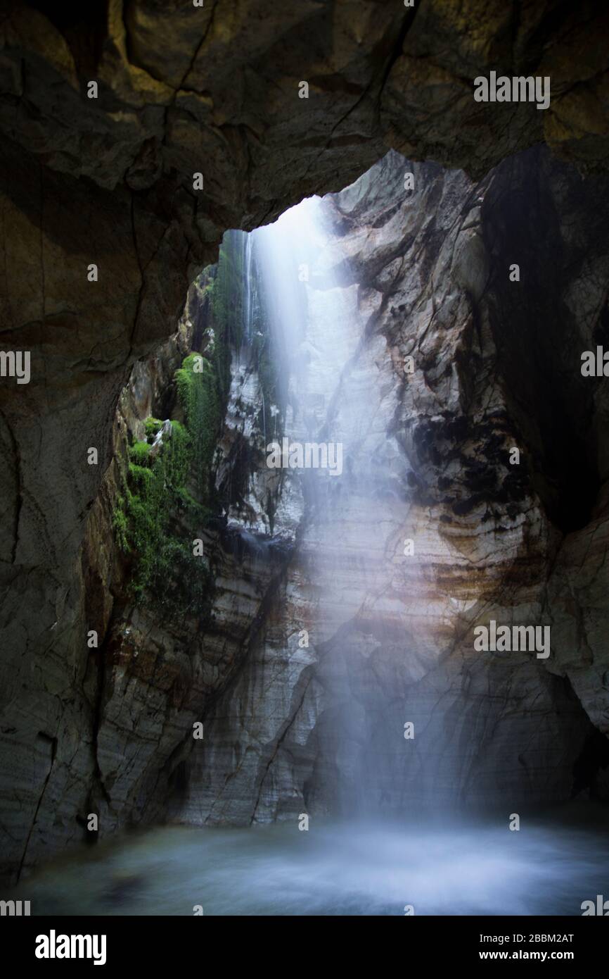 Luce che splende attraverso la cascata in un'antica grotta Foto Stock