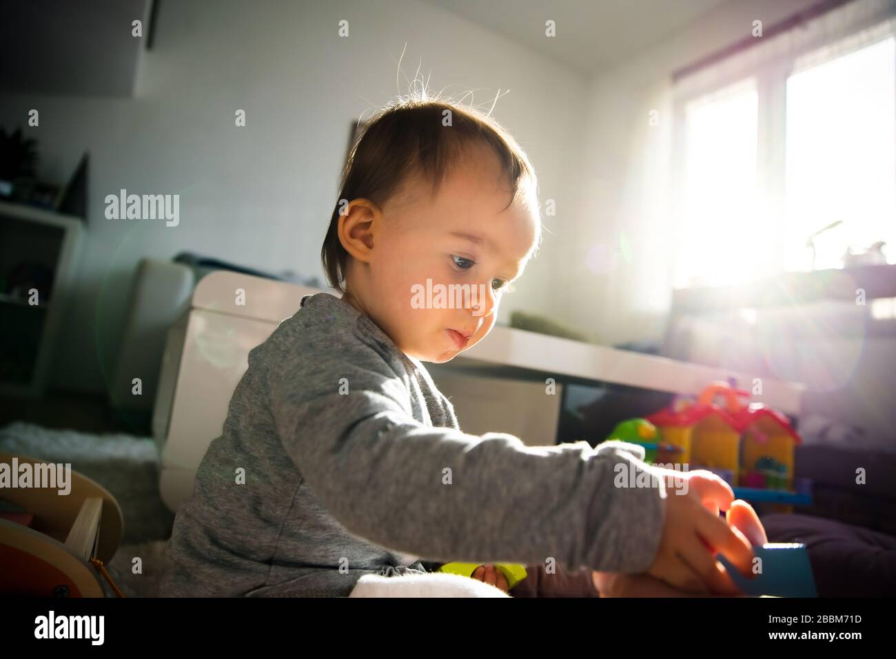 Ritratto di una bambina di un anno all'interno in una stanza luminosa giocando da sola Foto Stock