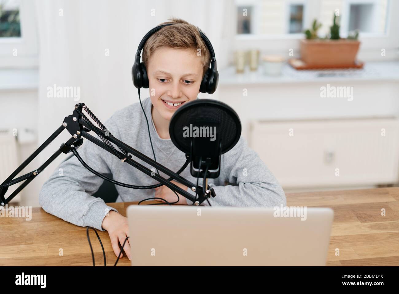 Ragazzo adolescente in cuffie seduto al tavolo con computer portatile di  fronte al microfono professionale con filtro pop, la registrazione della  sua voce Foto stock - Alamy