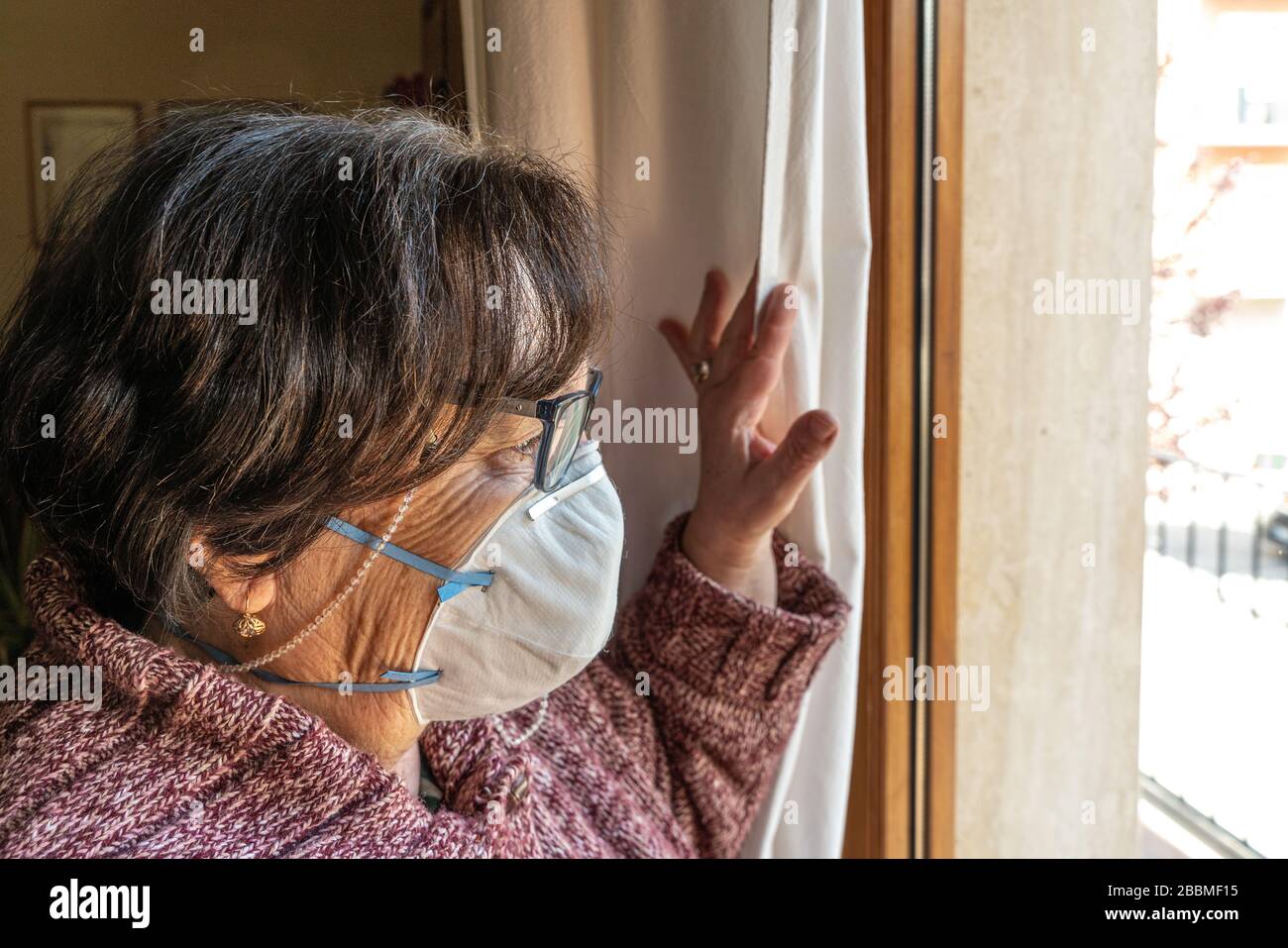 la quarantena delle donne anziane con maschera facciale guarda fuori la finestra Foto Stock