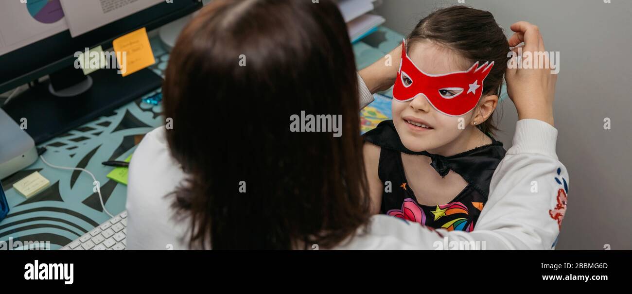 Donna telelavoro e mettere maschera costume su sua figlia Foto Stock