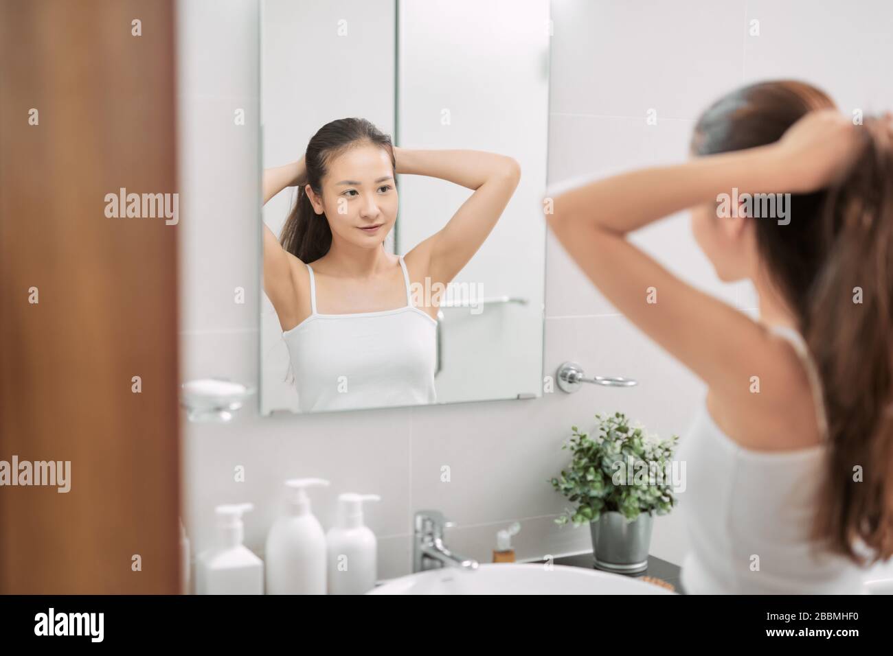 Donna in bianco vestaglia vestaglia che lega i suoi capelli davanti allo  specchio nella foto di bagno luminoso Foto stock - Alamy