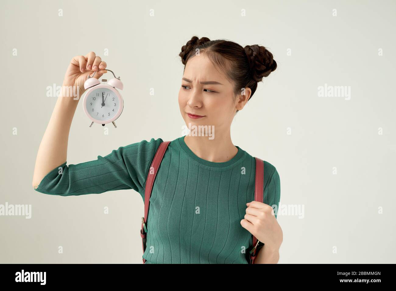La giovane donna asiatica si sente confusa e incerta, dubita di un aspetto perplesso che tiene un orologio Foto Stock