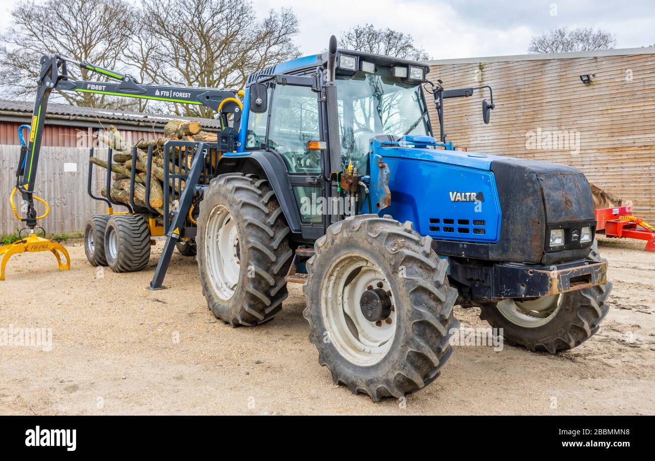 Grande trattore blu finlandese Valtra 6550 con cabina e 4 grandi ruote gommate, con un rimorchio pieno di tronchi di pino abbattuto, Surrey, Inghilterra sud-orientale Foto Stock