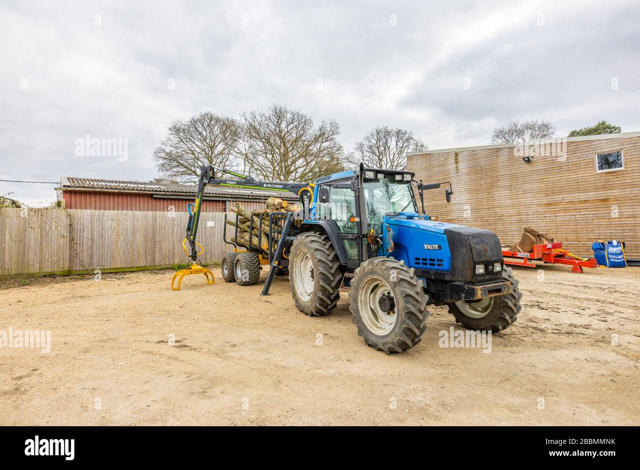 Grande trattore blu finlandese Valtra 6550 con cabina e 4 grandi ruote gommate, con un rimorchio pieno di tronchi di pino abbattuto, Surrey, Inghilterra sud-orientale Foto Stock