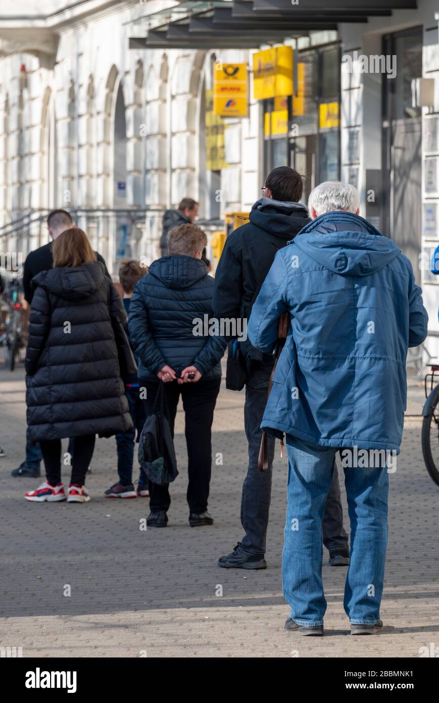 Magdeburg, Germania. 27th Mar, 2020. Una lunga coda si è formata di fronte ad un ufficio postale nel quartiere Stadtfeld. La gente sta mantenendo una distanza minima di due metri a causa della crisi del Corona. Ciò dovrebbe ridurre il rischio di contrarre il virus. Credito: Stephan Schulz/dpa-Zentralbild/ZB/dpa/Alamy Live News Foto Stock