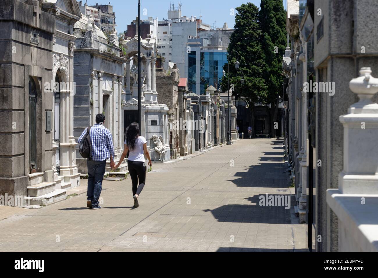 Uomo e donna che tengono le mani mentre camminano attraverso le tombe che costeggiano le strette strade del cimitero la Recoleta nel centro di Buenos Aires Foto Stock
