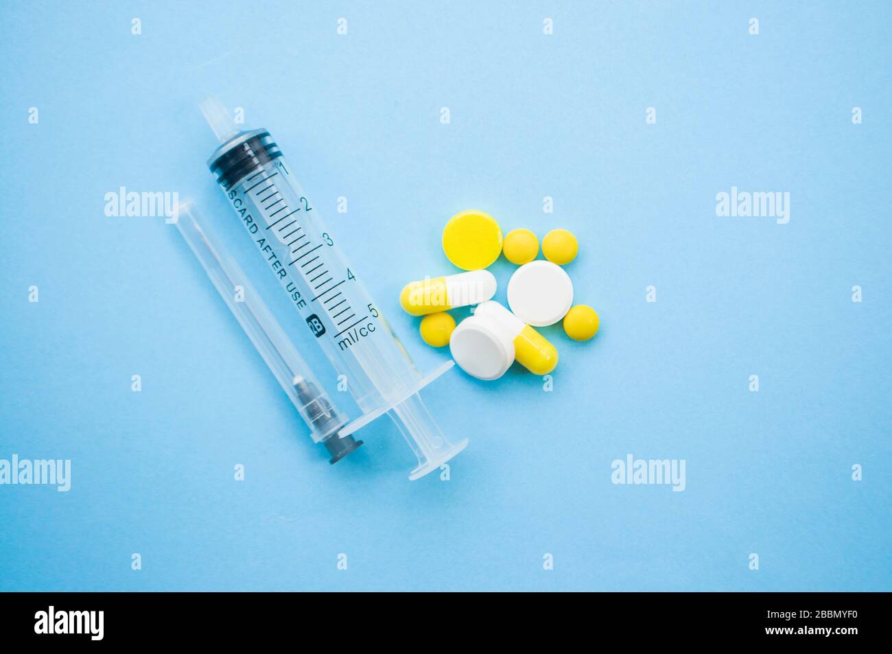 Pillole gialle, capsule, compresse, siringa e ago su sfondo blu. Stop coronavirus Concept. Proteggetevi. Foto Stock