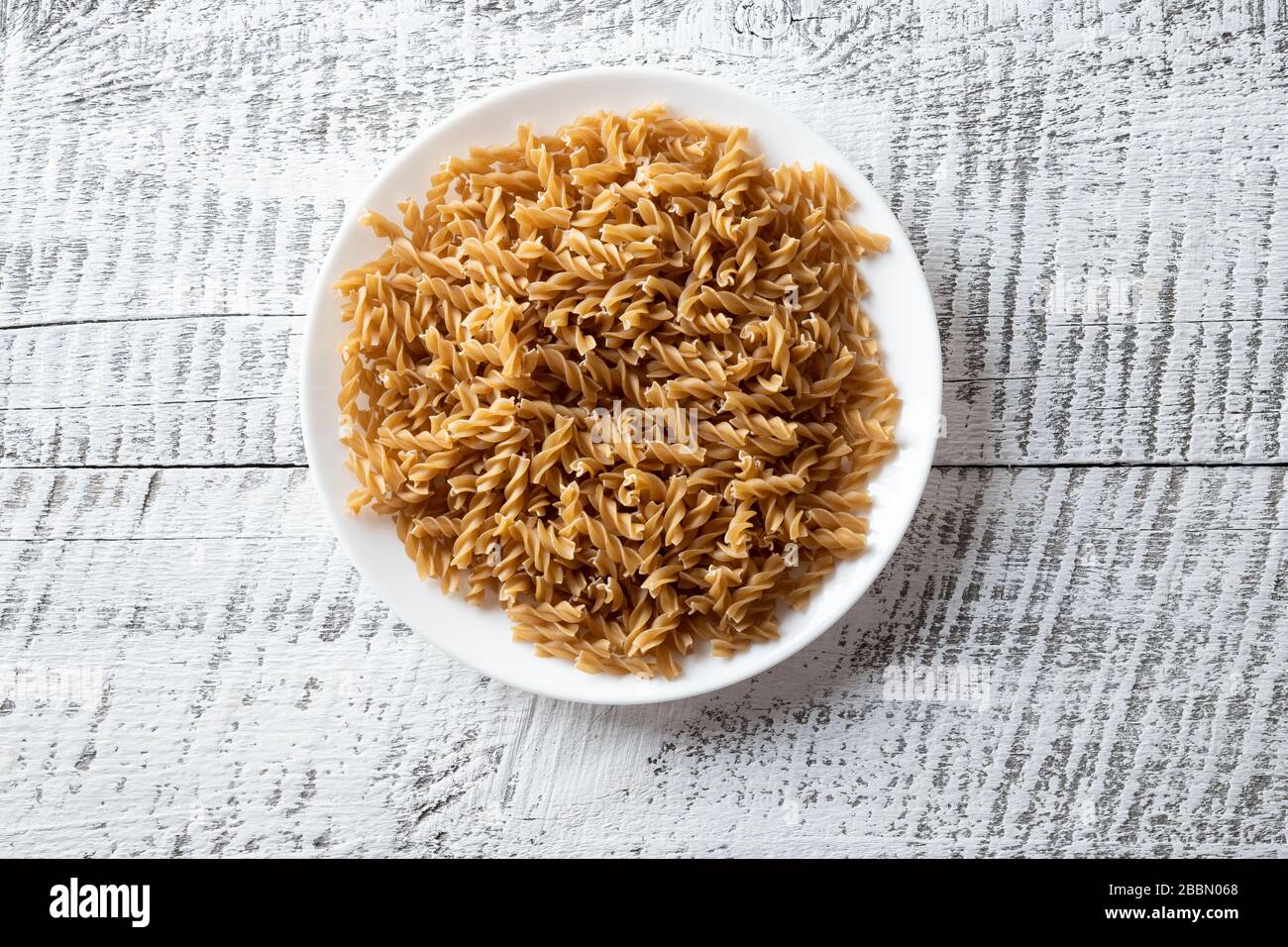 Fusilli a forma di farro integrale su lastra su sfondo di legno bianco. Foto Stock