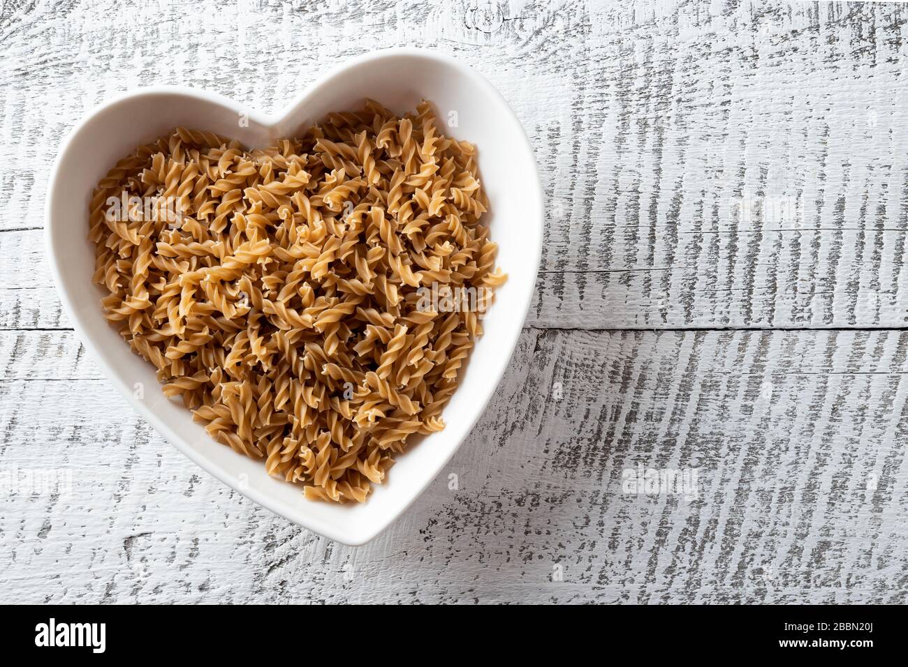Fusilli a forma di farro integrale su lastra su sfondo di legno bianco. Foto Stock