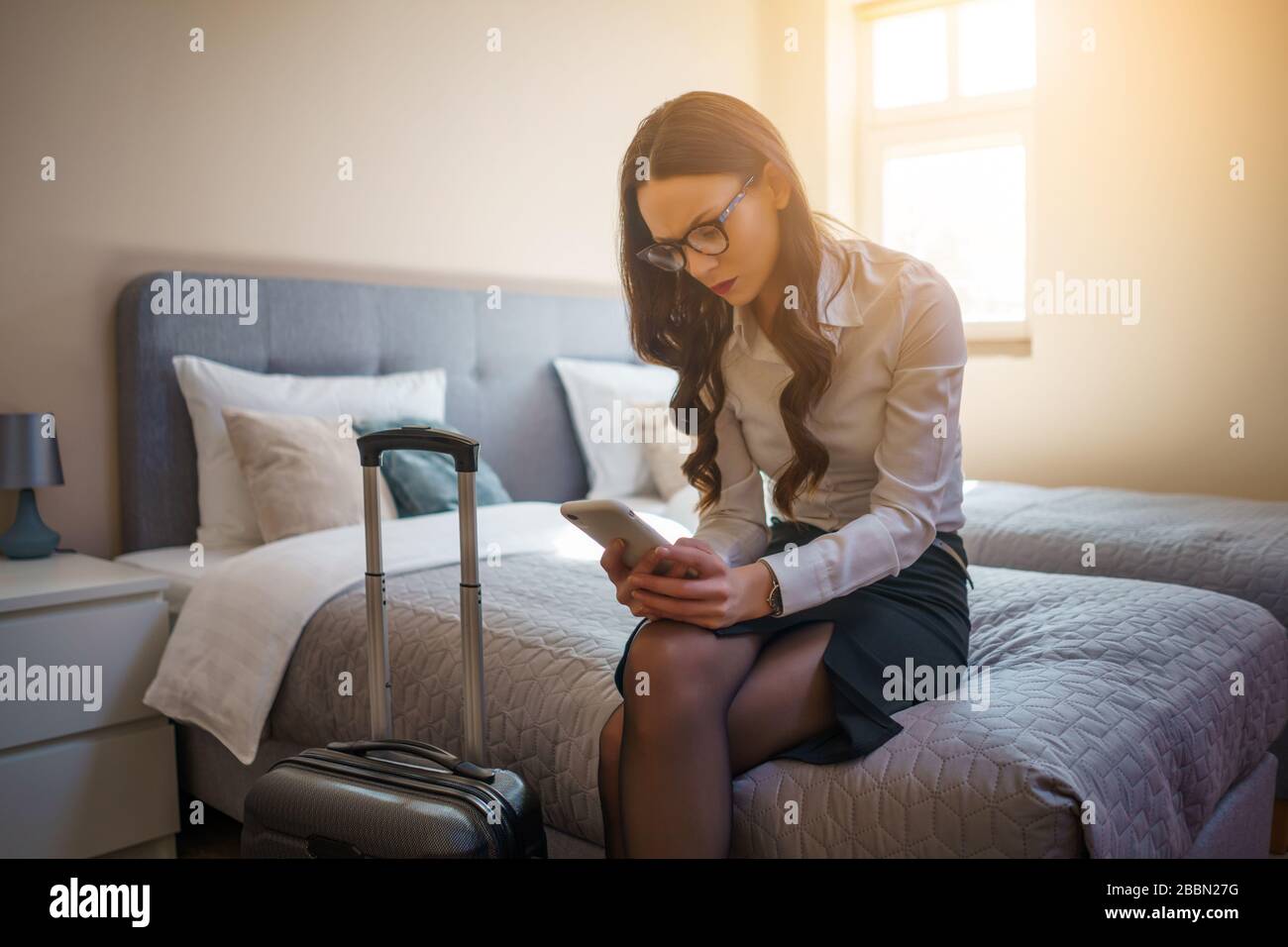 Donna d'affari stanco in viaggio d'affari seduto sul letto in camera d'albergo. Foto Stock
