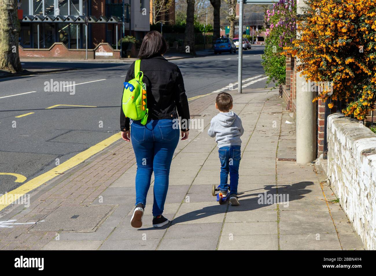 Una madre che cammina a fianco di un bambino in sella a uno scooter sul marciapiede Foto Stock