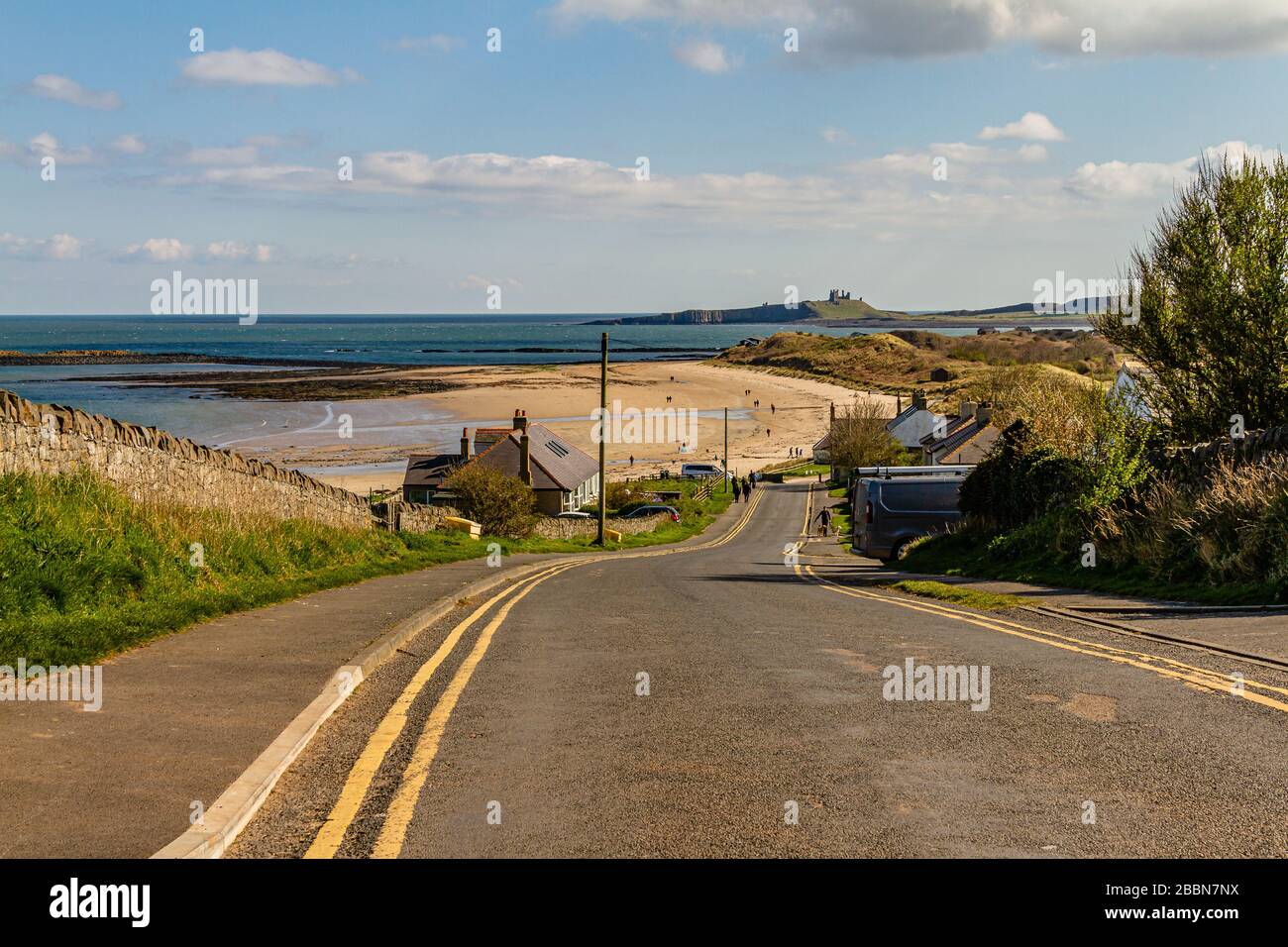 Si scende verso il villaggio e la spiaggia, con vista sul castello di Dunstanburgh. Basso Newton-by-the-Sea, Northumberland, Regno Unito. Aprile 2019. Foto Stock