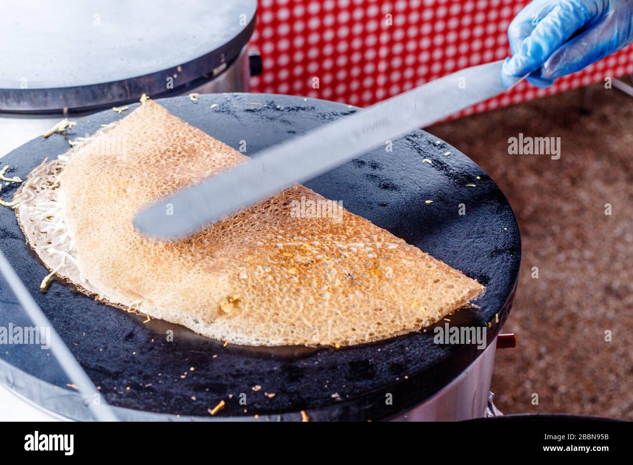 Fare crepes frittelle in un mercato alimentare. Una mano sta facendo crepes saporite all'aperto su una griglia di metallo. Foto Stock