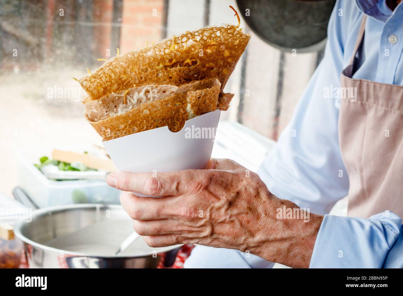 Fare crepes frittelle in un mercato alimentare. Una mano serve crepes saporite con formaggio fuso e funghi all'aperto in una stalla alimentare. Foto Stock