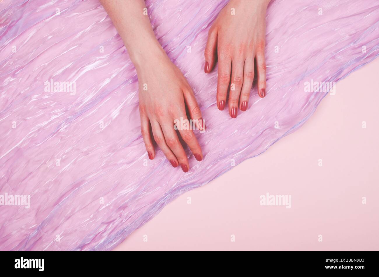 Donna mani con manicure e sciarpa in tessuto satinato su sfondo rosa Foto Stock