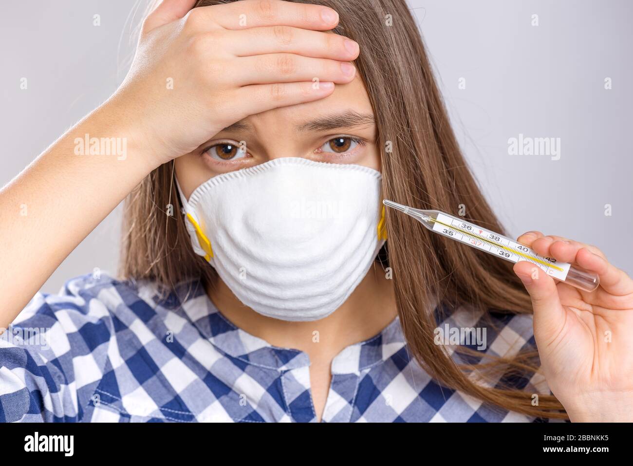 Concetto di quarantena del coronavirus. Sick bambino che indossa una maschera protettiva per uso medico con termometro ad alta temperatura. COVID-19 - isolamento domestico. Foto Stock