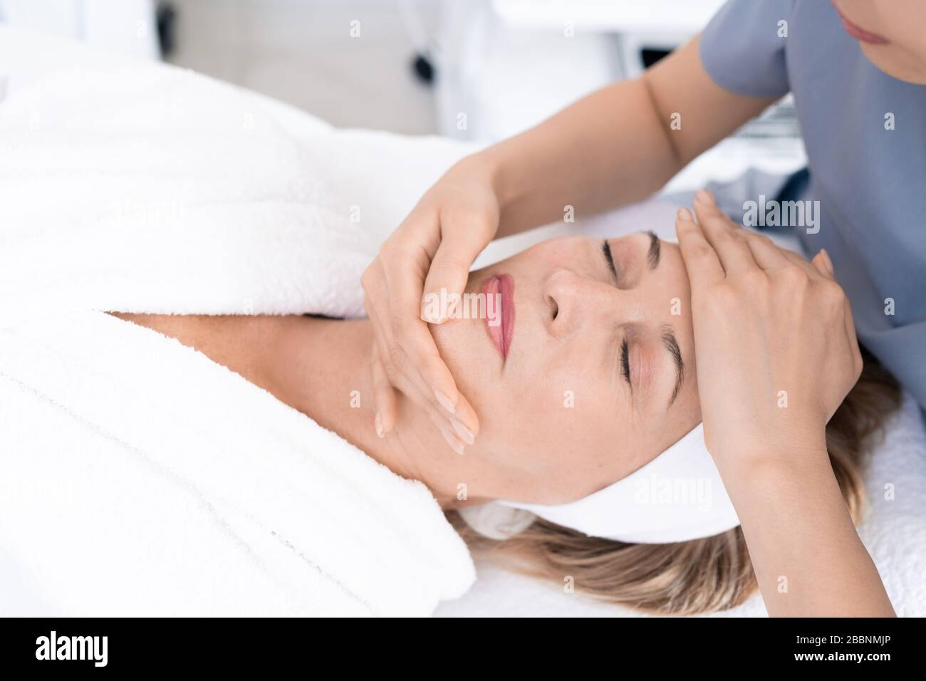 Primo piano di estetica professionale scolpitura viso di donna matura con massaggio, donna rilassata godendo di trattamento di bellezza procedura Foto Stock