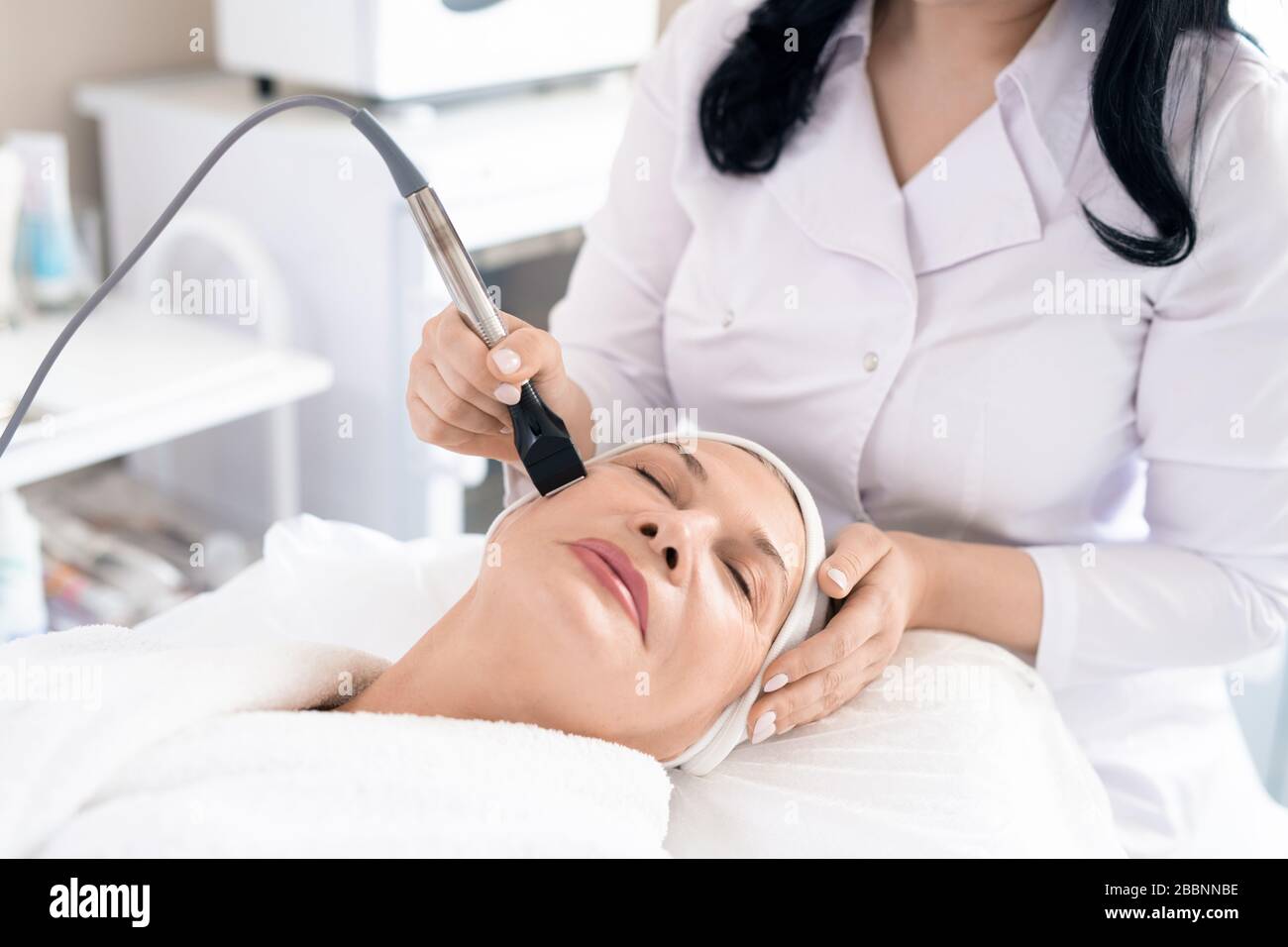 Primo piano di colmetologo che tiene la procedura di peeling viso a donna matura in salone di bellezza Foto Stock