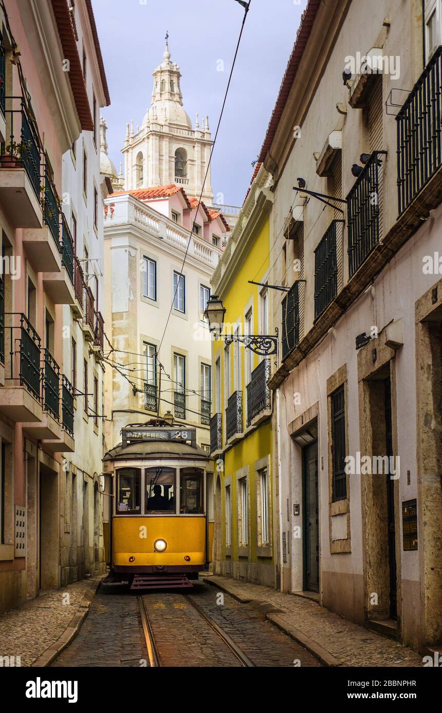 Strada stretta nel centro storico di Lisbona con tipico tram giallo elettrico Foto Stock