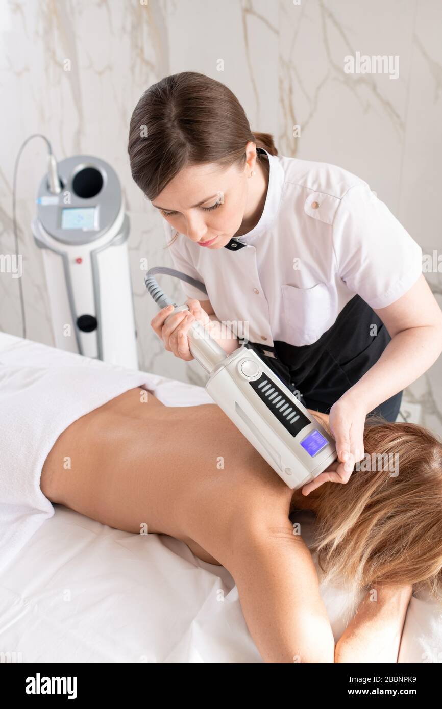 Giovane terapista massaggiante la schiena della donna con massaggiatore corpo per rilassare i muscoli nella procedura di trattamento di bellezza Foto Stock