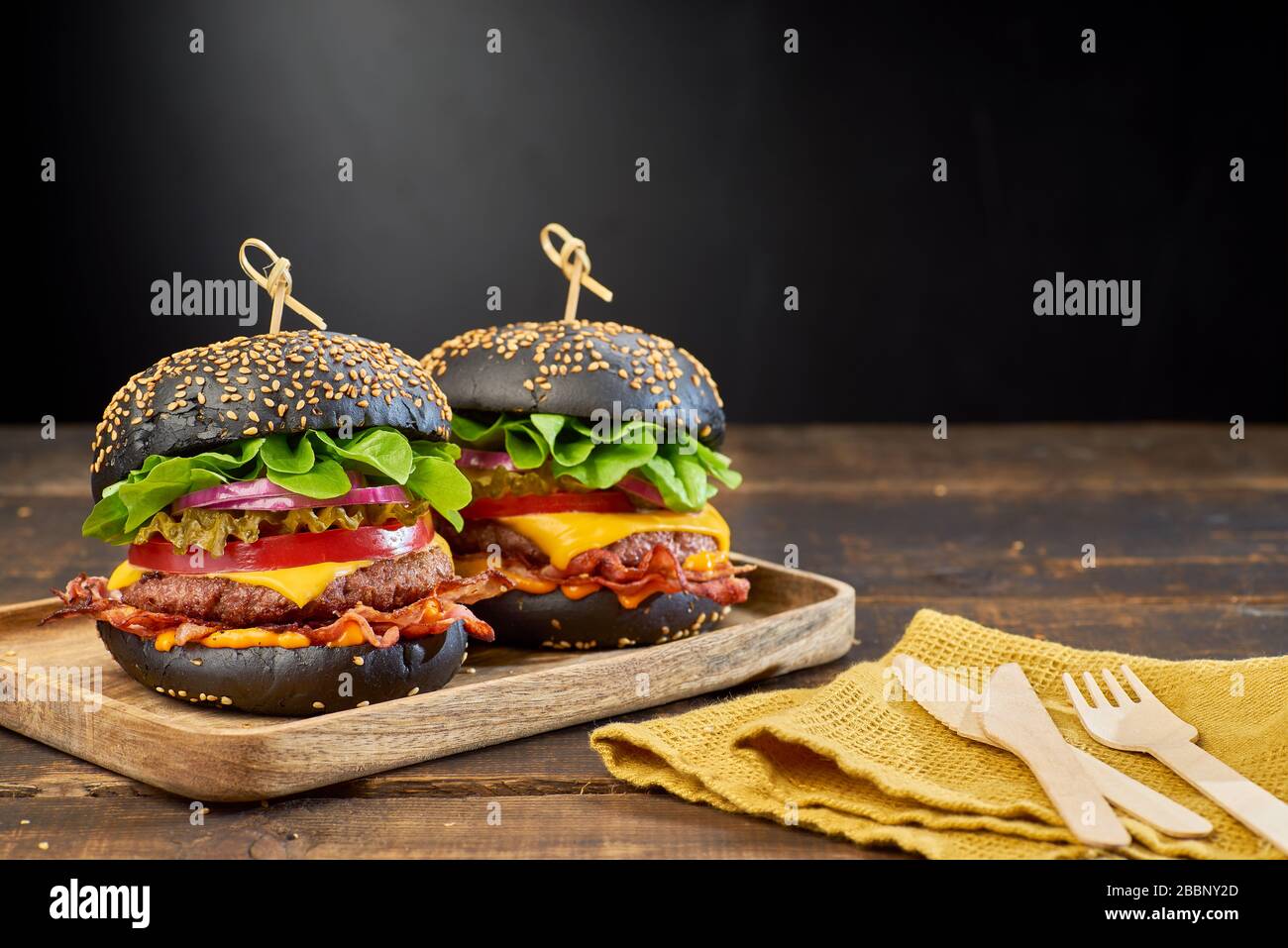 Due hamburger neri su sfondo di legno scuro Foto Stock