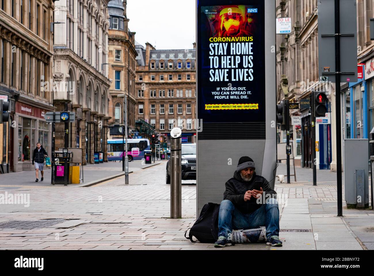 Glasgow, Scozia, Regno Unito. 1° aprile 2020. Effetti del blocco Coronavirus sulle strade di Glasgow, Scozia. Il senzatetto si siede sotto il video schermo con il consiglio di salute di Coronavirus. Iain Masterton/Alamy Live News Foto Stock