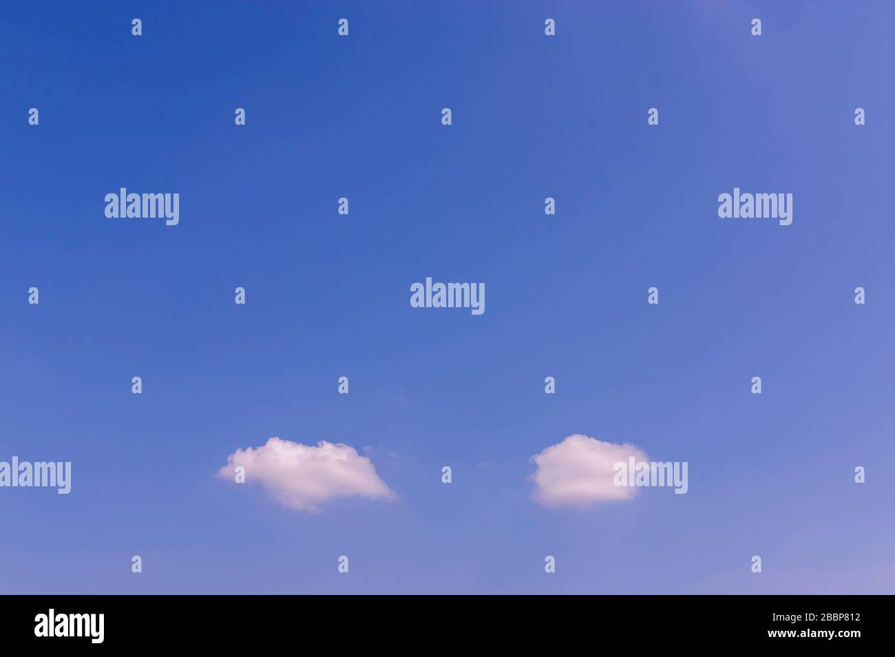 Cielo blu al sole con due piccole nuvole bianche, come nuvole di pensiero o bolle vocali, con molto spazio di copia Foto Stock