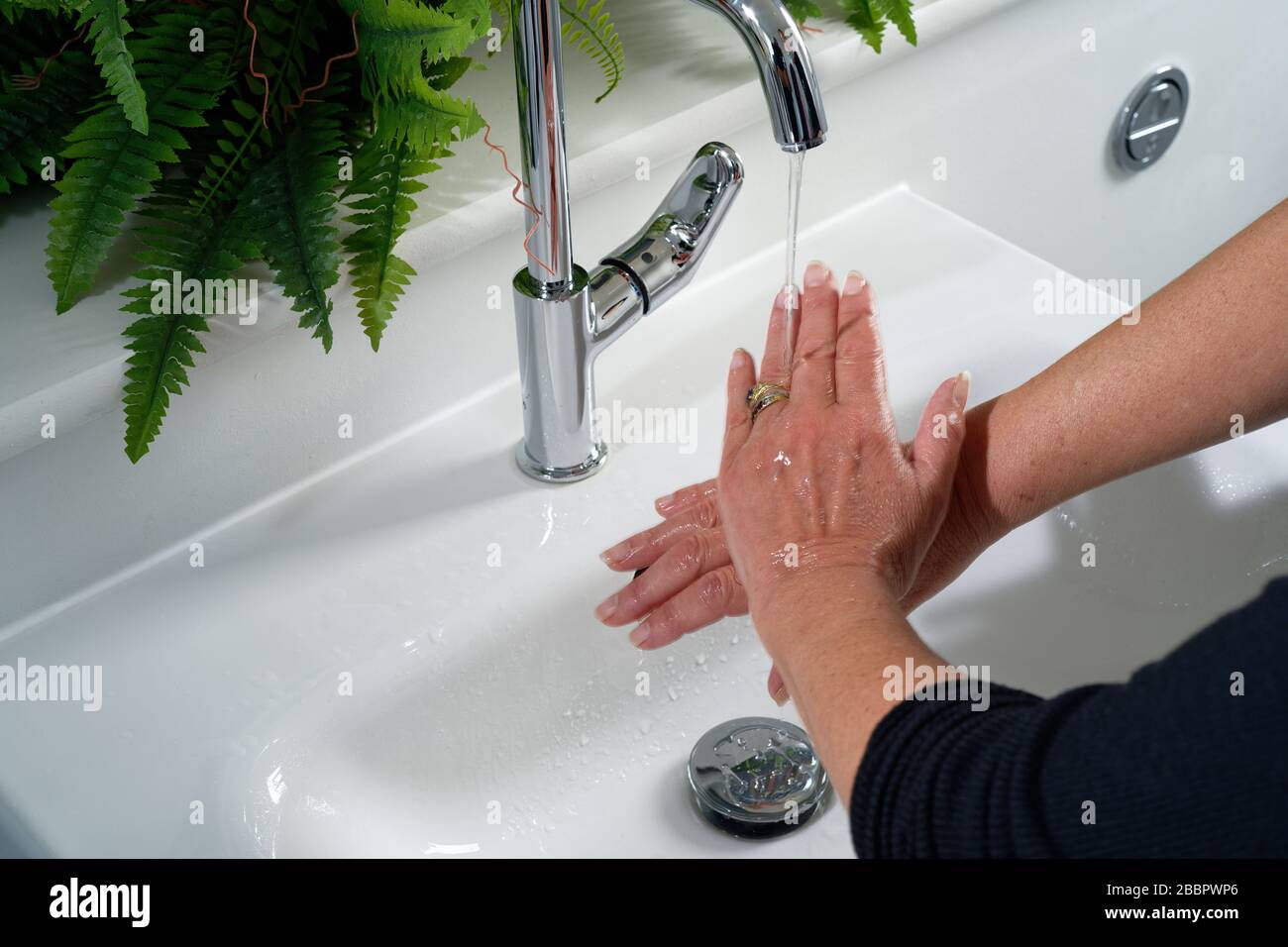 Una donna che lavava le mani in un lavandino domestico. Picchiettare con acqua che scorre sulle mani e conca dietro. Stanza da bagno o stanza da bagno. Foto Stock