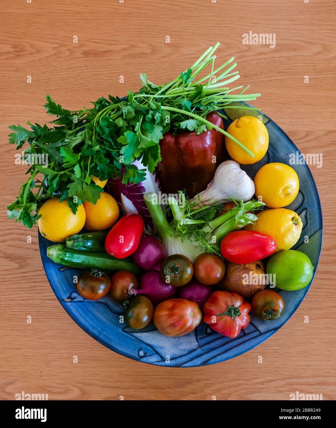 Variopinto recipiente di frutta e verdura fresca: Cicoria, erba di prezzemolo, cipolle, zucchine, finocchio, pomodori, limoni, lime, pepe e aglio Foto Stock