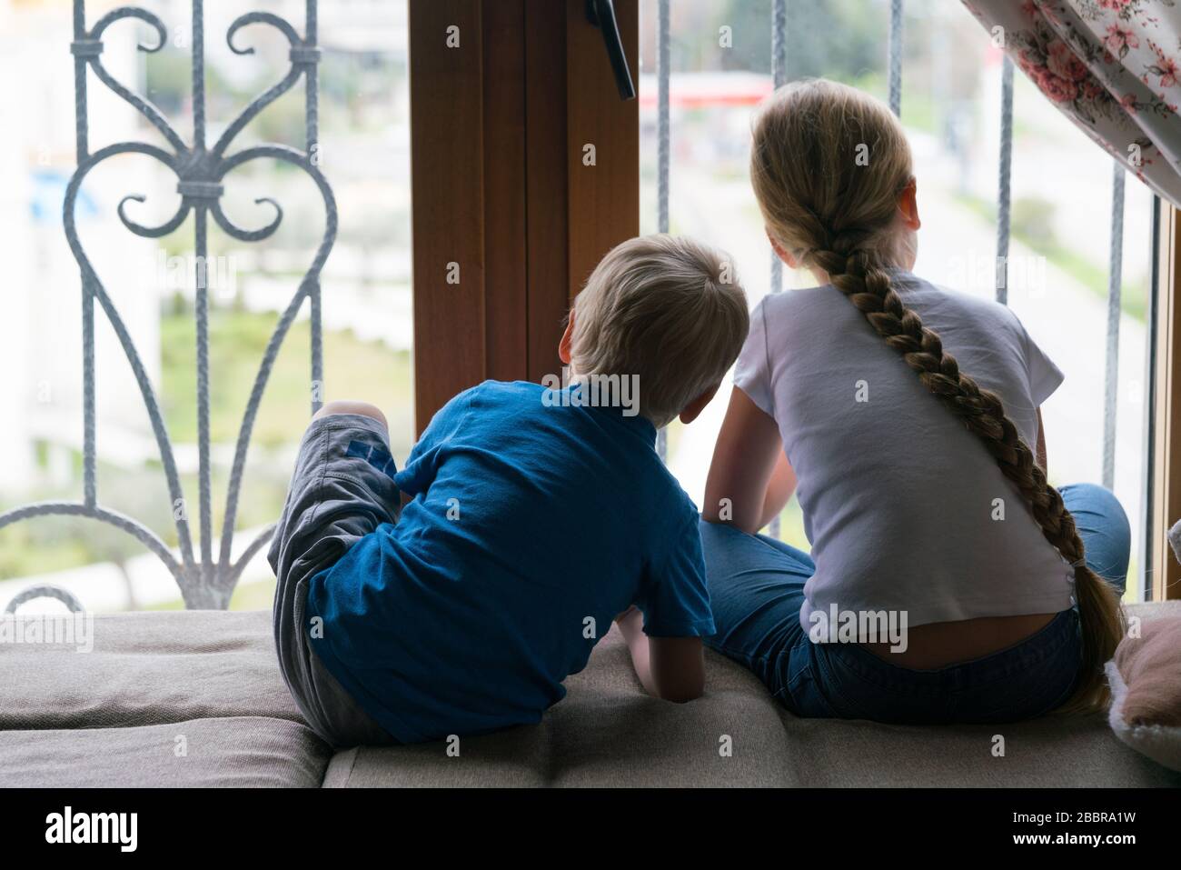 Rimanere a casa quarantena coronavirus pandemic prevenzione, fratello e sorella guardando fuori la finestra non in grado di uscire per una passeggiata Foto Stock