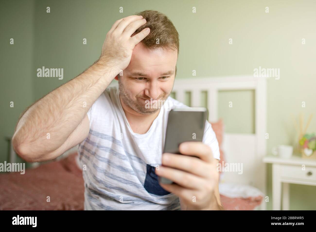 Giovane uomo che si preoccupa mentre tiene il telefono o lo smartphone in mano. Una mano nella testa. Grande concetto troble faccia. Foto Stock