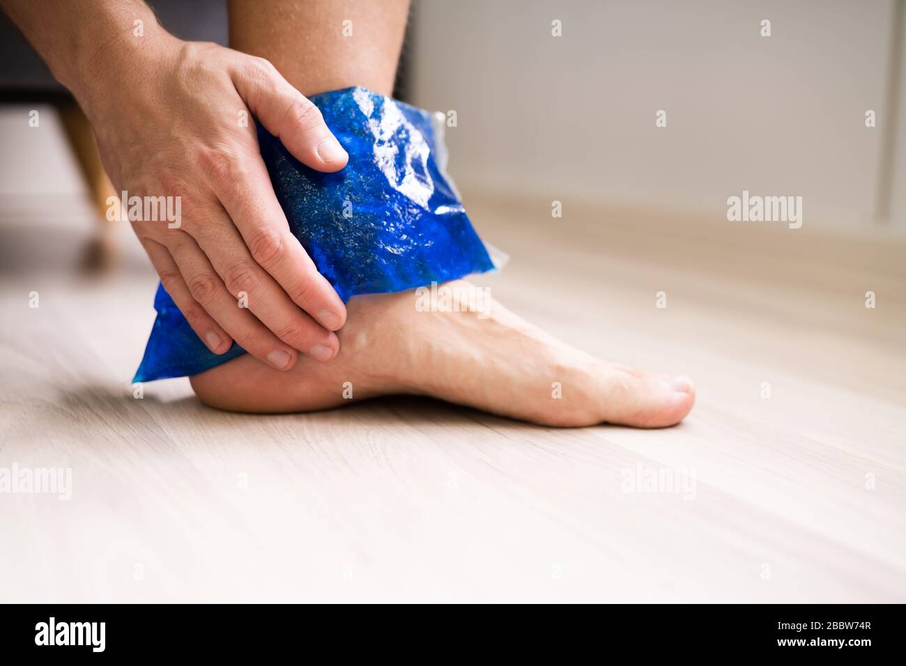 Close-up di persona della mano che tiene il gel del ghiaccio Pack su caviglia a casa Foto Stock