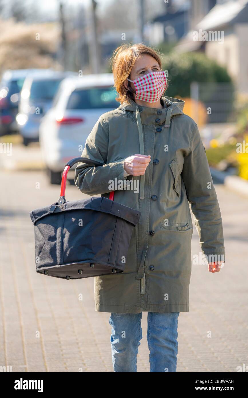 Donna va a fare shopping, indossa una maschera respirante, cucita da sé, fatta di cotone, effetti della crisi corona in Germania Foto Stock