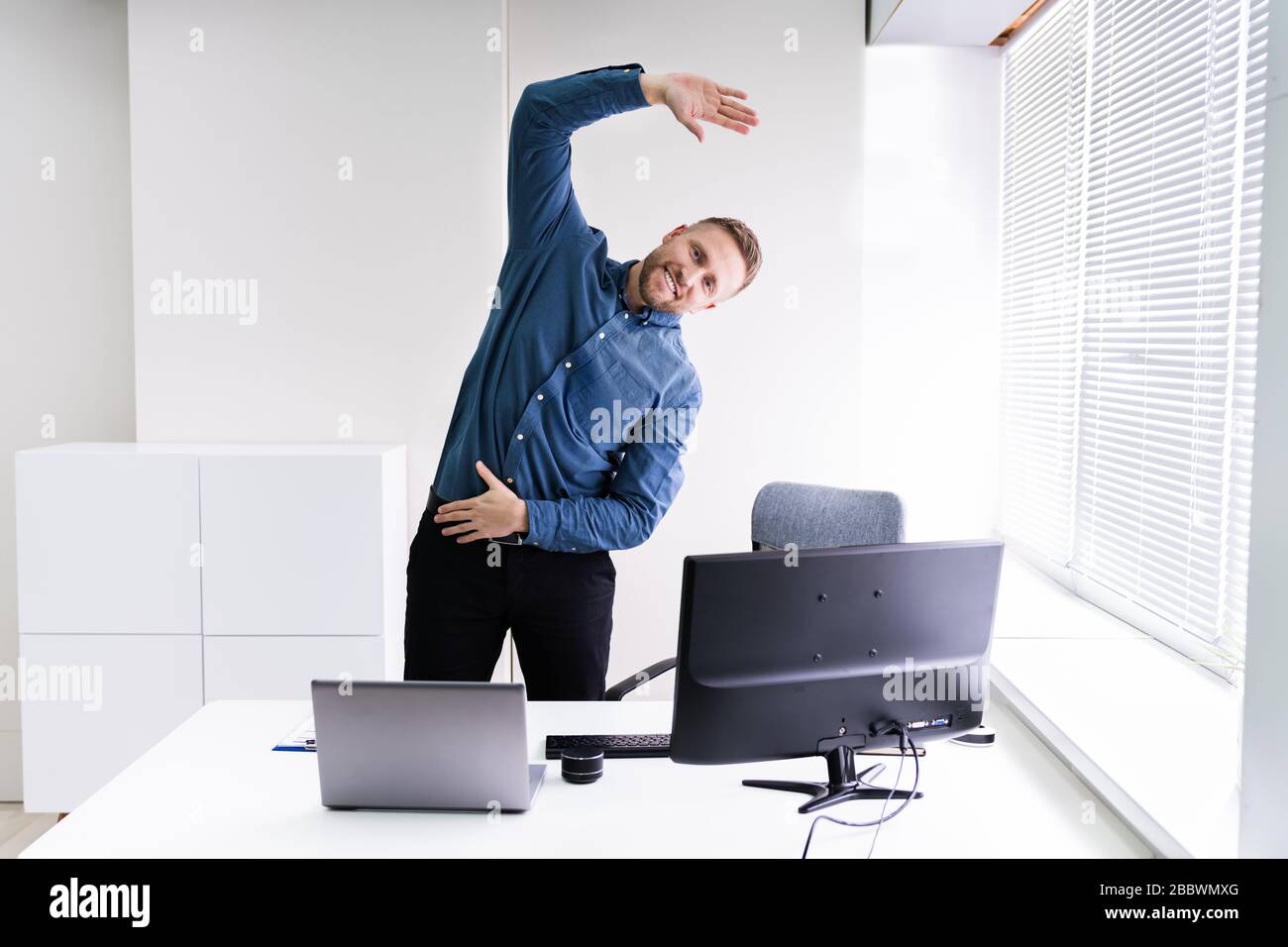 Giovane Imprenditore facendo esercizio di stretching in ufficio Foto Stock