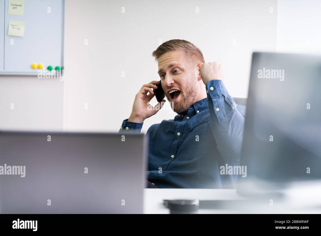 Uomo d'affari sorridente che guarda via mentre comunica sul cellulare in ufficio Foto Stock