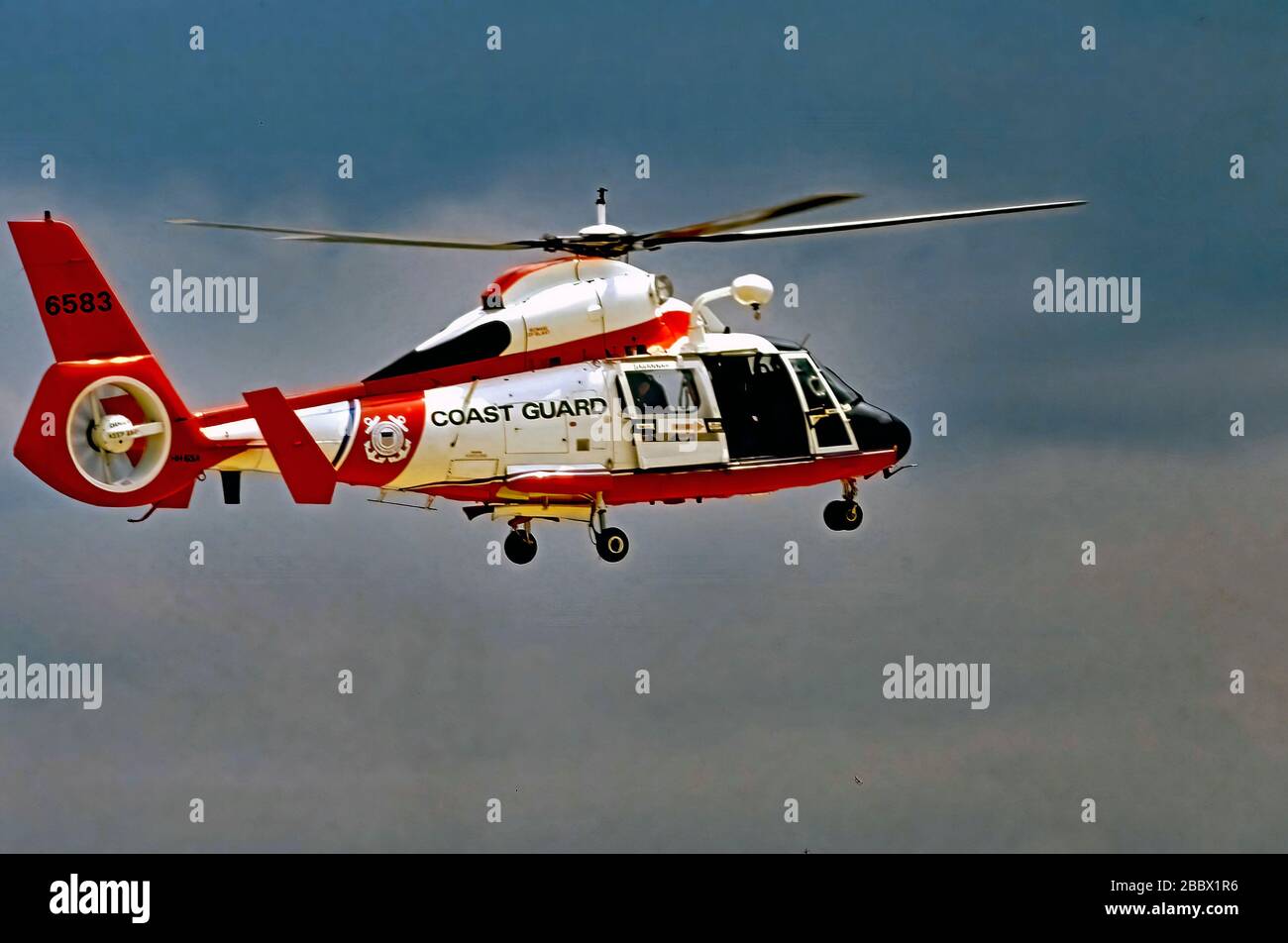 Camp Springs Maryland, Stati Uniti, 20 maggio 1989 A United States Coast Guard MH-65 Dauphin Short Range Recovery elicottero passa alla modalità hover mentre il nuotatore di salvataggio sul retro si prepara a schierare l'imbracatura di sollevamento come parte di una dimostrazione delle capacità dell'Airbus fabbricato elicottero che la Guardia Costiera utilizza per varie missioni, tra cui Ora dotato di mitragliatrici versione (MH-65Cs) per proteggere il Campidoglio degli Stati Uniti Foto Stock