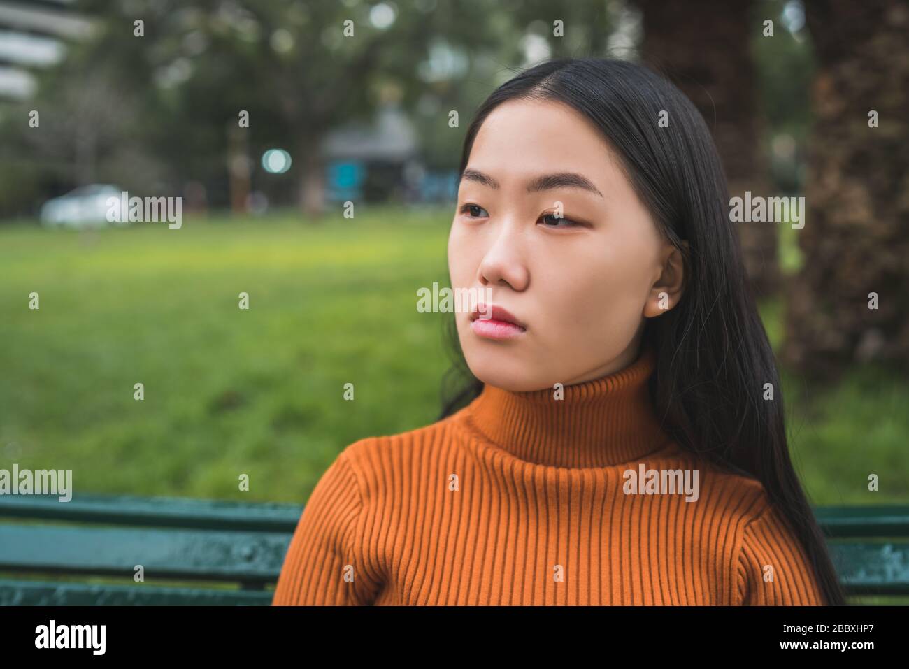 Ritratto di giovane bella donna asiatica seduta su una panchina nel parco all'aperto. Foto Stock