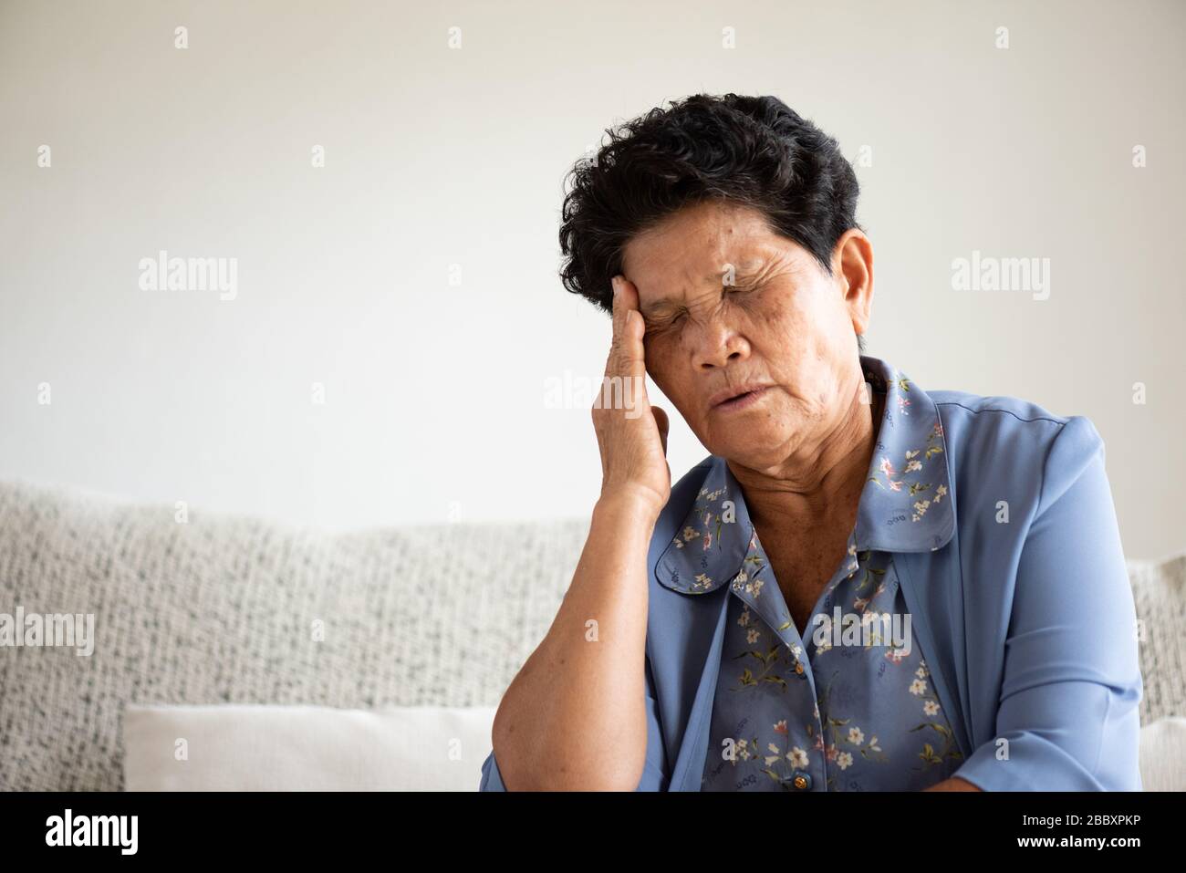 Vecchia donna asiatica seduta sul divano e avere un mal di testa a casa. Concetto di assistenza sanitaria di alto livello. Foto Stock