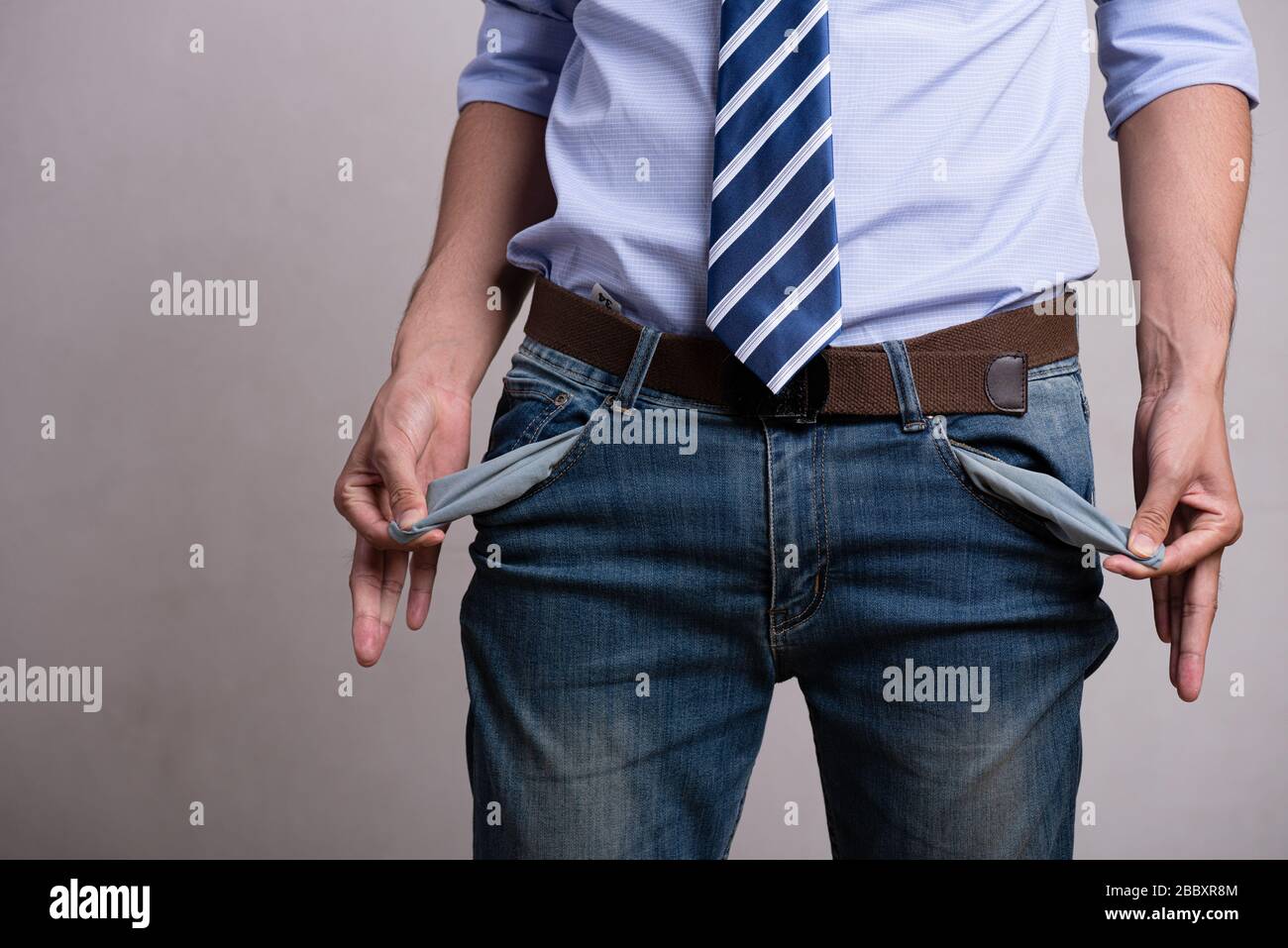 Un giovane uomo d'affari in un vestito da lavoro che mostra le sue tasche vuote. Difficoltà finanziarie, cattiva economia, nessun concetto di denaro. Foto Stock